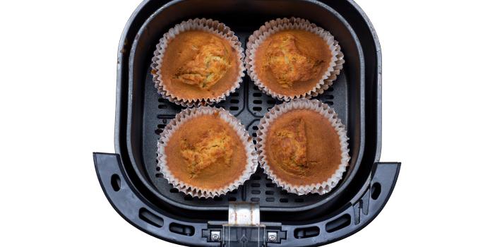 Fotografia vista de cima de quatro muffins de banana sem glúten dentro da cestinha da air fryer, a qual está sobre um fundo branco.