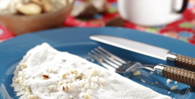 fotografia em tons de azul, branco e vermelho de uma bancada forrada com um pano vermelho e por cima um prato redondo azul com a tapioca e garfo e faca ao lado para servir.