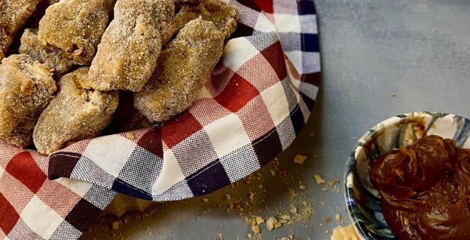 Foto da receita de paglia de doce de leite servida em diversas porções em uma cesta com um pano quadriculado vermelho e preto sobre uma mesa cinza, com um bowl de porcelana com doce de leite ao lado.