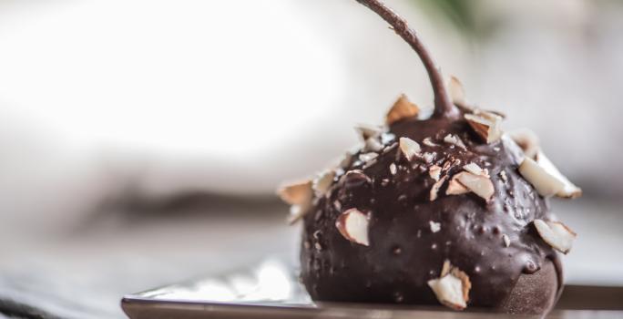 Fotografia de uma pera coberta com chocolate à base de Neston e lascas de nozes sobre um prato de vidro de cor clara.
