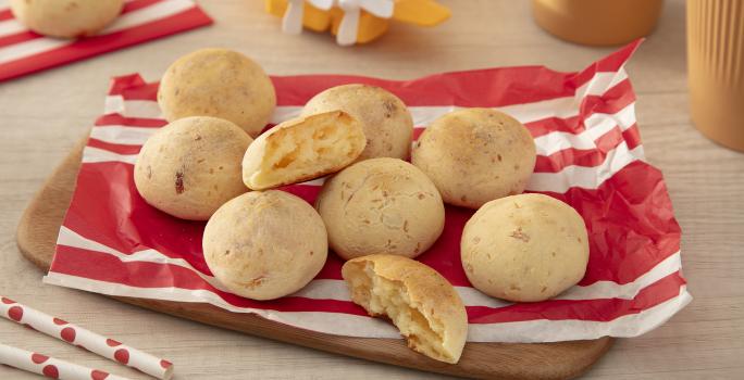 Fotografia em tons de vermelho com vários pães de queijo feitos com NINHO Primeira Infância ao centro.