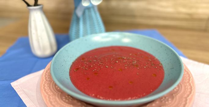 Fotografia em tons de rosa e azul com um prato azul ao centro. Dentro do prato existe uma receita de sopa de legumes com ASCENDA