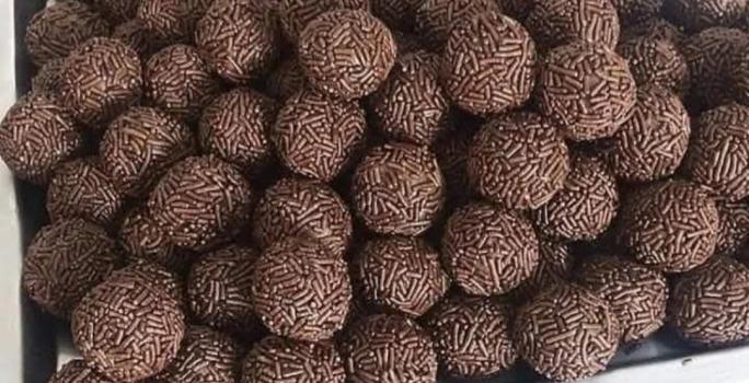 Fotografia de vários brigadeiros de café passados no granulado tradicional. Os brigadeiros estão dentro de uma forma grande retangular de alumínio.