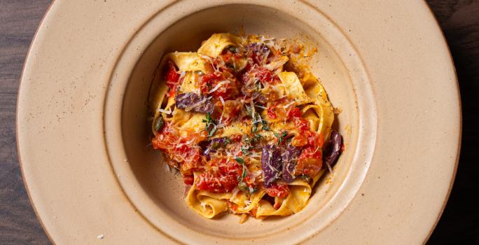 Fotografia em tons de bege com um prato de macarrão talharim ao centro. Por cima do macarrão existe um molho de tomates com anchovas e alcaparras.