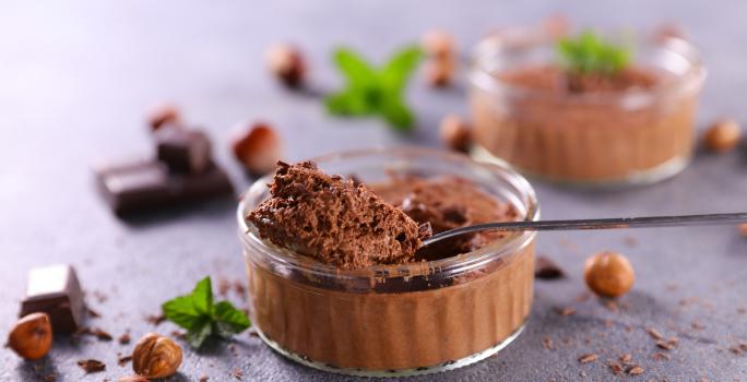 Fotografia em tons de azul com um pote de vidro ao centro. Dentro do pote existe uma mousse de chocolate feita com nescau