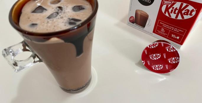 Fotografia em tons de vermelho com uma caneca de vidro ao centro. Dentro da caneca existe uma receita de Iced Mocha feita com Dolce Gusto Kitkat. Nas bordas da caneca existe uma calda de chocolate