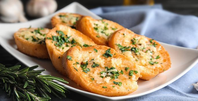 Fotografia em tons de branco com um prato branco ao centro. Em cima do prato existe uma receita de rabanada salgada com ervas e queijo parmesão