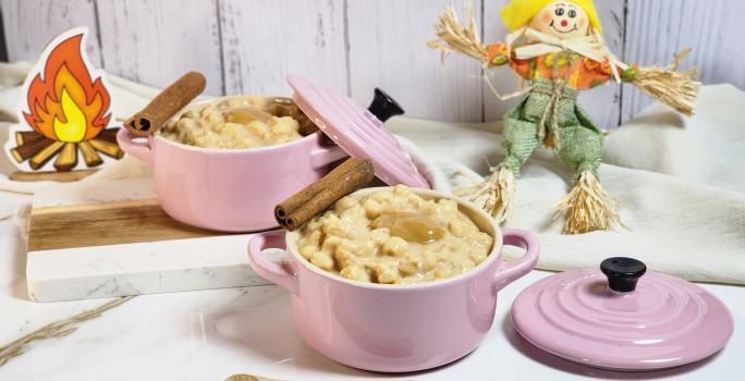 Foto de uma cena com dois potes rosas com a canjica de doce de leite dentro, alguns paus e canela decorado, pequenos espantalhos decorativos ao fundo, tudo sobre uma bancada de mármore branca com tecidos