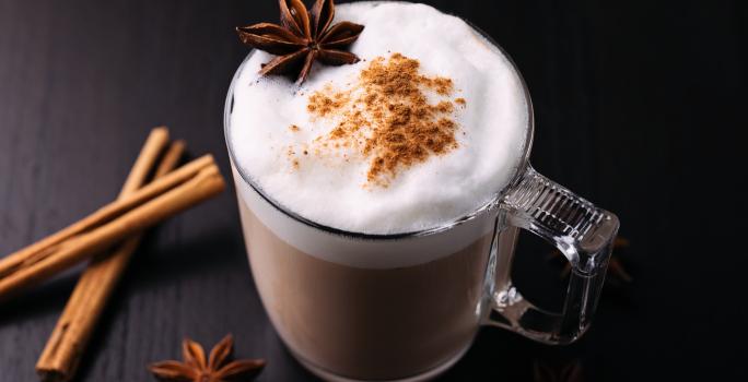 Fotografia de uma xícara de vidro com uma bebida quente com leite MOÇA, chocolate em pó, NESCAFÉ, leite, cravo, canela.