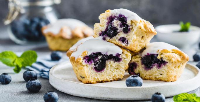 Fotografia em tons de branco com três bolinhos cupcakes ao centro. Os cupcakes são feitos com blueberries e cobertura de limão.