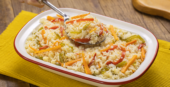 Fotografia mostra uma travessa com arroz com pimentões coloridos e uma colher servindo arroz.