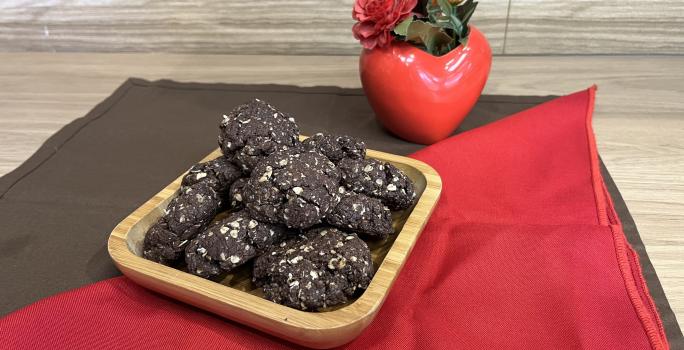 Fotografia em tons de vermelho e marrom com um recipiente de madeira ao centro. Dentro do recipiente existe vários cookies de NESCAU com NESTLÉ Aveia Flocos!