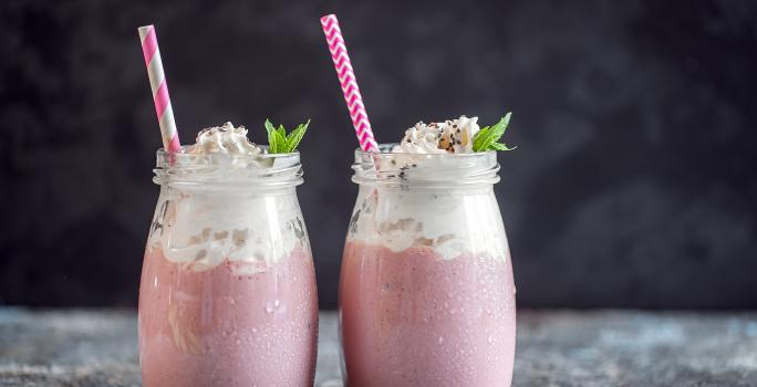 Fotografia de dois recipientes decorativos de vidro com frapê com Leite MOÇA, guaraná e suco de limão. No mesmo copo tem um canudo rosa e branco e hortelã.